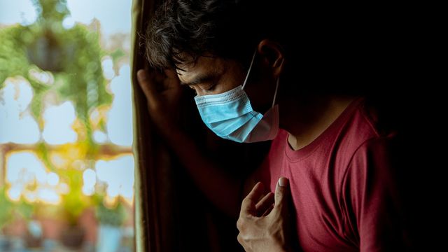 A man holding his chest while wearing a face mask. 