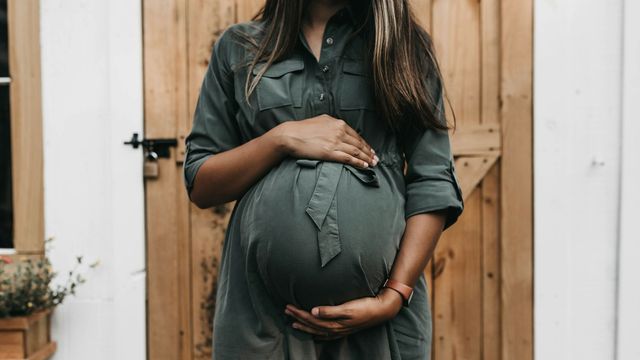 A pregnant person holds their belly with both hands. 