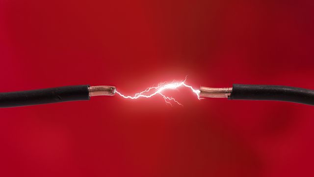 Electricity traveling in the space between two cables with exposed ends on a red background. 