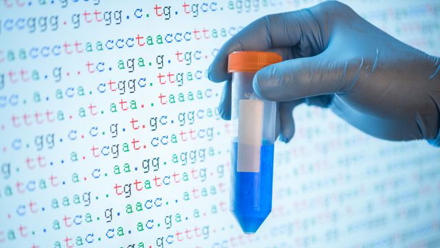 A hand holding a centrifuge tube in front of a screen with DNA bases. 