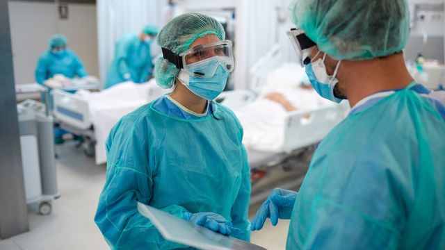 Two healthcare professionals wear personal protective equipment while talking. 