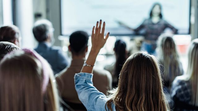 A lady raising her hand in a talk to ask a question. 