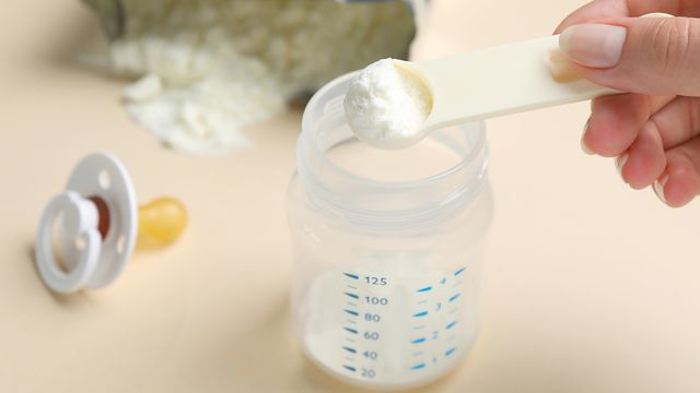 Woman preparing infant formula on beige background, closeup. Baby milk 