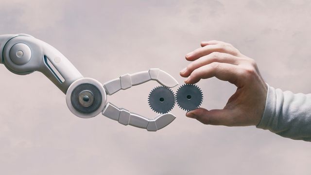 A robot arm holding a gear touching a human hand also holding a gear 