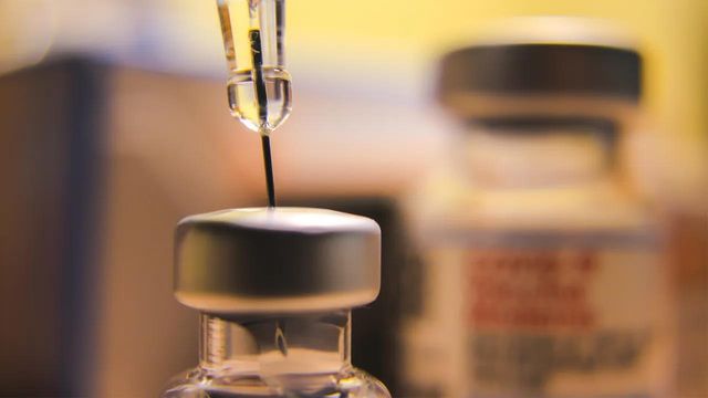 Close-up of a syringe drawing liquid from a vial, with the needle inserted into the vial's rubber stopper, blurred background 